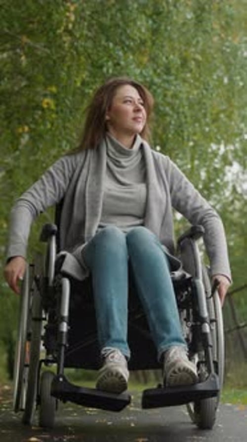 Woman with Injury Moves Turning Wheels of Wheelchair in Park