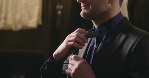 A man in a tailor shop and tailor-made clothes tries a suit and knots his tie and holds it to work