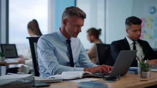 Smiling businessman enjoys coffee while working on laptop in bright open office