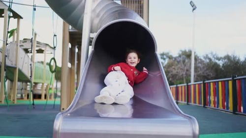 A Happy Child Sits at the Top of a Slide in a Playground Ready for Fun and Adventure