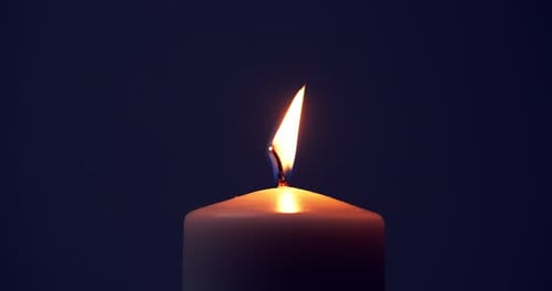 Single big yellow candle flame lights and extinguish, isolated on a black background. Slow motion an