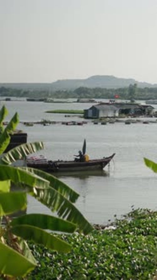 Feuilles de palmier sur les rives du lac Tri an au Vietnam où un homme asiatique conduit un bateau rempli de sacs de