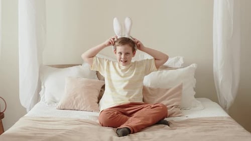 Adorable Caucasian Boy Puts White Plush Bunny Ears on Head at Home