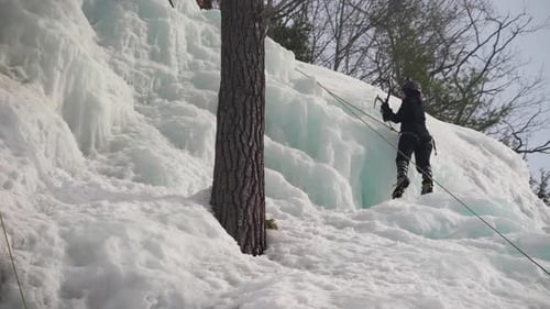 A woman ice climbing their way up a snow and ice covered mountain