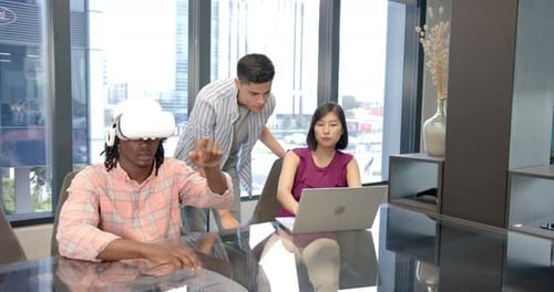 Using VR headset, man collaborating with colleagues working on laptop in office