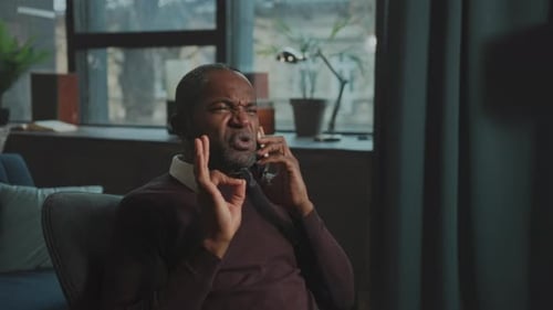 El hombre discute apasionadamente El hombre se sienta animadamente discutiendo y gesticulando durante un teléfono cargado de emociones