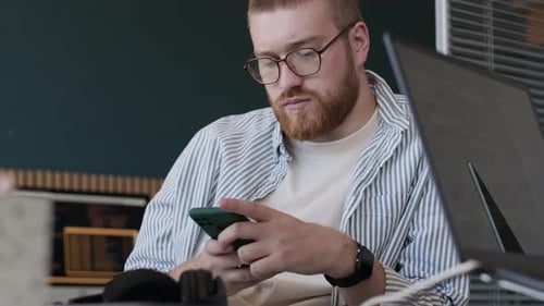 Bearded Young Man Using App On Smartphone At Work