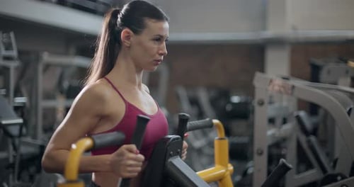 A Young Beautiful Brunette Girl in Sportswear is Exercising on a Machine in the Gym Doing Exercises