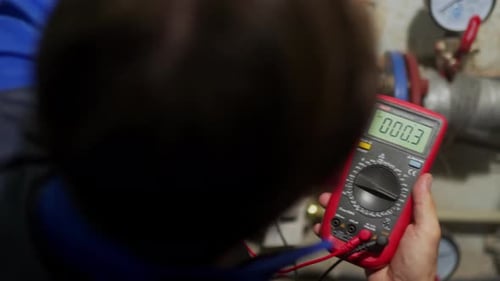 Electrician Checking Voltage in a Fuse Box with Multimeter in District Heating Substation Master in