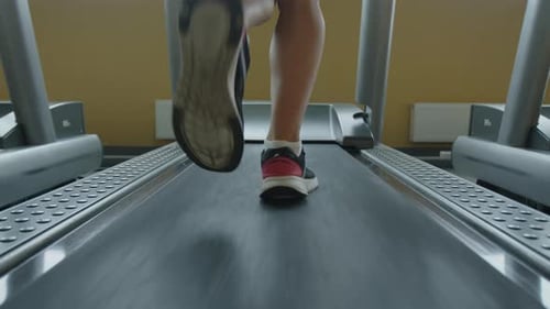 Back View of Sporty Female Athlete Running on a Treadmill in a Fitness Gym