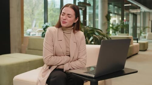 Disappointed Caucasian Businesswoman Using Laptop and Feeling Sudden Stomach Ache in Office Lobby
