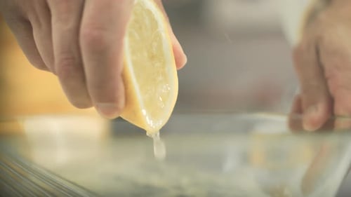 Nahaufnahme einer Zitrone, die von einem veganen Koch gepresst wird, bis Zitronensafttropfen in eine Glasschale fallen.
S