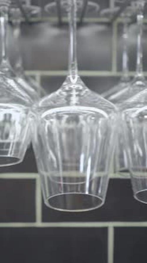 Slide Shot of Different Wine Glasses Hanging By Dark Tile Wall at Bar