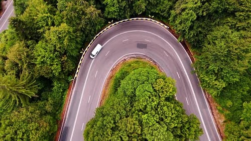Vehicle navigating a winding road through lush forest.