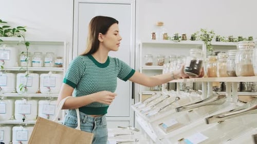Una mujer joven está comprando en una tienda de recarga con bolsas reutilizables y sin residuos.