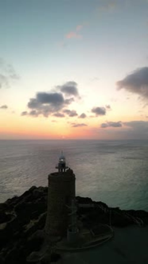 vertical Aerial drone view approaching lighthouse on sea cliffs at sunset