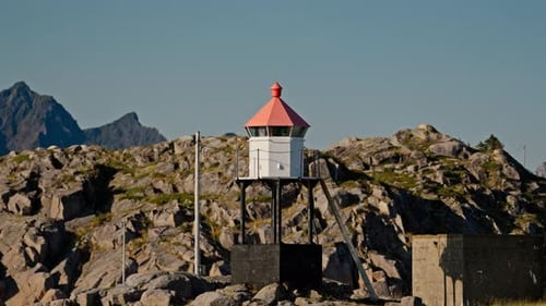 Coastal Lighthouse on Rocky Shoreline with Mountain Backdrop