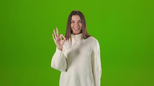 Frau zeigt Zeichen Ok mit Finger auf grünem Hintergrund