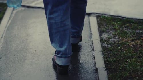 Pedestrian Crossing Rainslicked Urban Street Blue Jeans and Black Shoes Holding Plastic Bottle Wet
