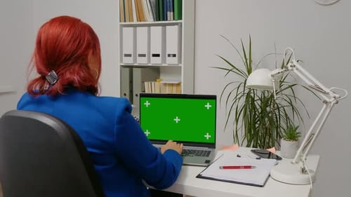 Business woman sitting working on laptop with mock up green screen display.