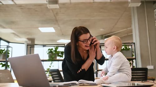Mother is working in the office, her little baby son is sitting on the table