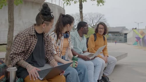College Friends Sitting with Laptops on Street Bench and Talking