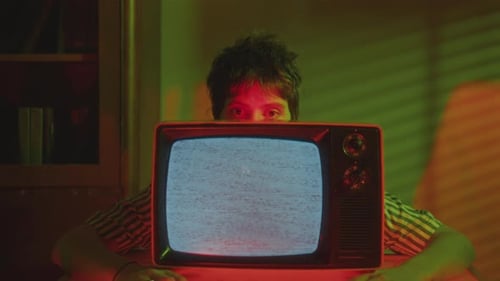 Junge Frau schaut im dunklen Raum hinter dem alten Analogfernseher hervor