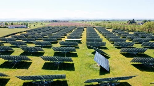 Rows of solar panels in a vast green field under a clear blue sky