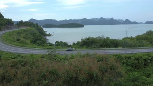 Scenic winding road with cars driving through lush tropical jungle overlooking the sea in Langkawi
