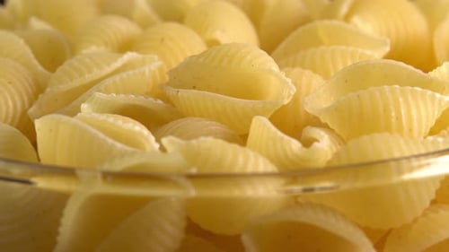Italian pasta conchiglie rigate shell shaped rotating in glass bowl side view. Durum wheat flour