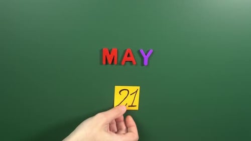 Hand sticking a sticker 21 May calendar day on school board. 21 date of May. Twenty first day
