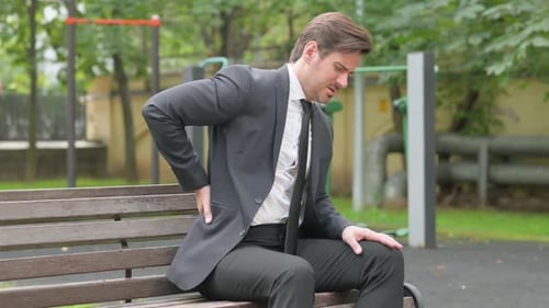 Man in Suit Experiencing Back Pain on Bench