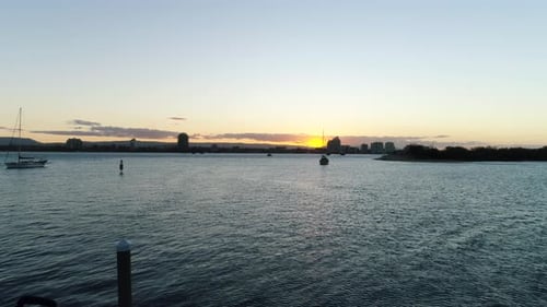 Aerial view of people fishing off jetty looking into an amazing sunset as a sail boat is parked on t