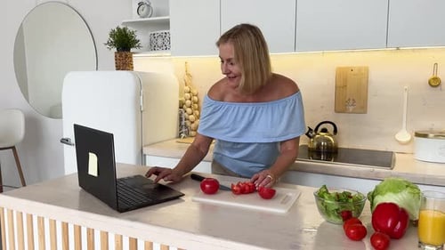 Woman Preparing Vegetables in Bright Kitchen With Laptop