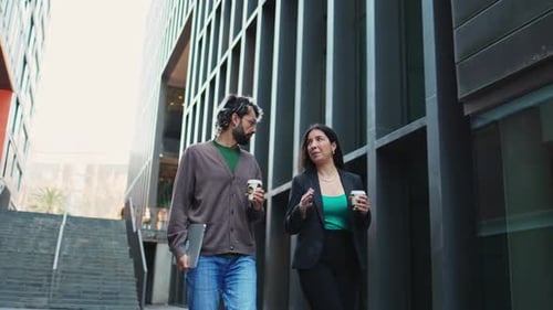 Zwei Geschäftsleute, die vor dem Büro spazieren gehen und lächeln, während sie mit Kaffee in der Hand sprechen