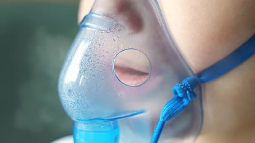 Vue rapprochée d'une petite fille assise et tenant un masque nébuliseur appuyé contre le visage