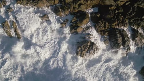 Top View Of Foamy Waves Breaking On The Rugged Shoreline. Aerial Shot