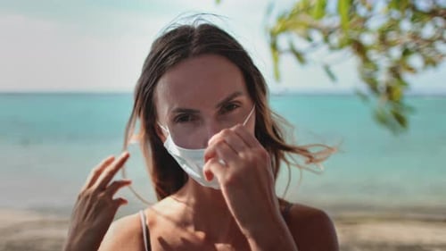 Woman on Beach Puts on a Surgical Mask