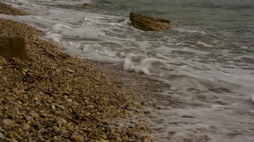 Close up of sea waves splashing on cliffs and pebbles beach in Ionian coastline