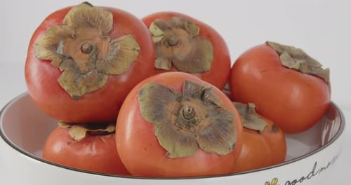 Nahaufnahme asiatischer Kakis in einer Schale mit Stängeln und leuchtenden Farben
