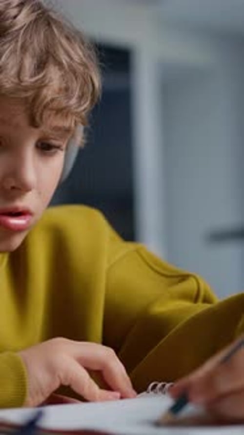 Focused Young Boy with Curly Hair Wearing a Yellow Sweater and Headphones Concentrating Carefully