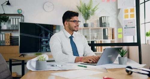 Man worker in glasses sitting in front of computer and typing on keyboard in modern office room