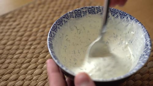 Mixing garlic sauce with a tablespoon. Garlic dip in a bright white and blue bowl on the wooden tabl
