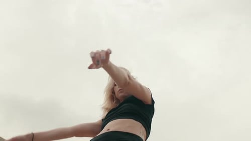 Junge Frau tanzt unter bewölktem Himmel