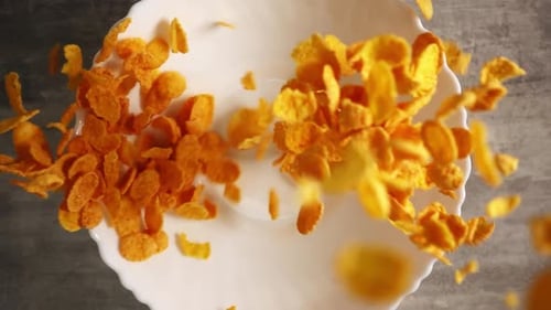 Bright Yellow Cornflakes for a Healthy Breakfast Fall Into a Plate Closeup and Scatter on the Table