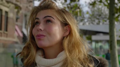 Confident beautiful young woman adjusts hair and sweater in the cool morning air. Close up portrait