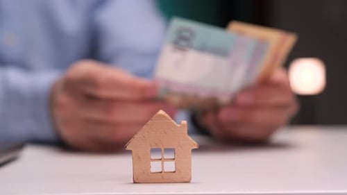 Businessman Counting Banknotes with Miniature House in the Foreground