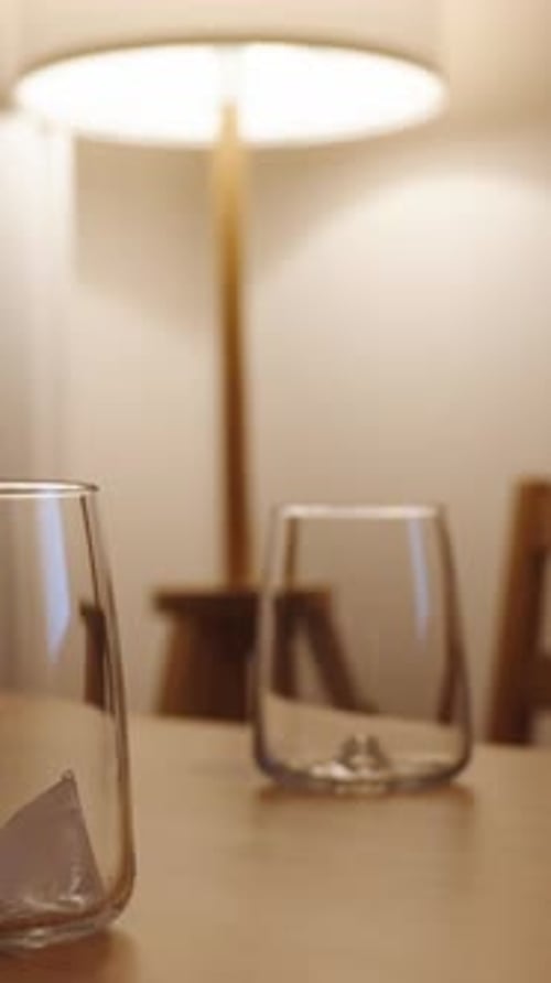 Vertical video. Two glasses with ice in the twilight, illuminated by warm light from a lamp.