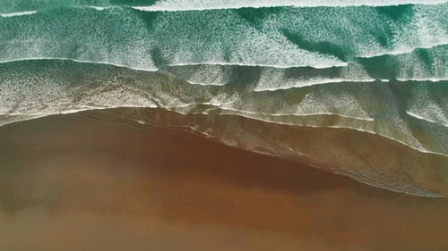 Aerial view of ocean waves meeting dark sandy beach