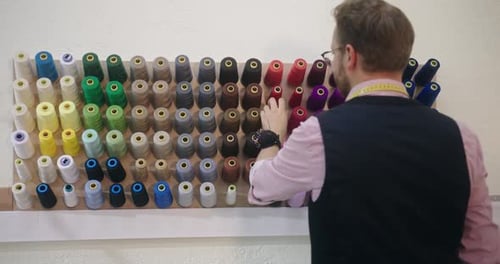 Schneider wählt das richtige Farbgarn aus, um sein Kleidungsstück aus einem an der Wand montierten Spulenständer zu nähen oder